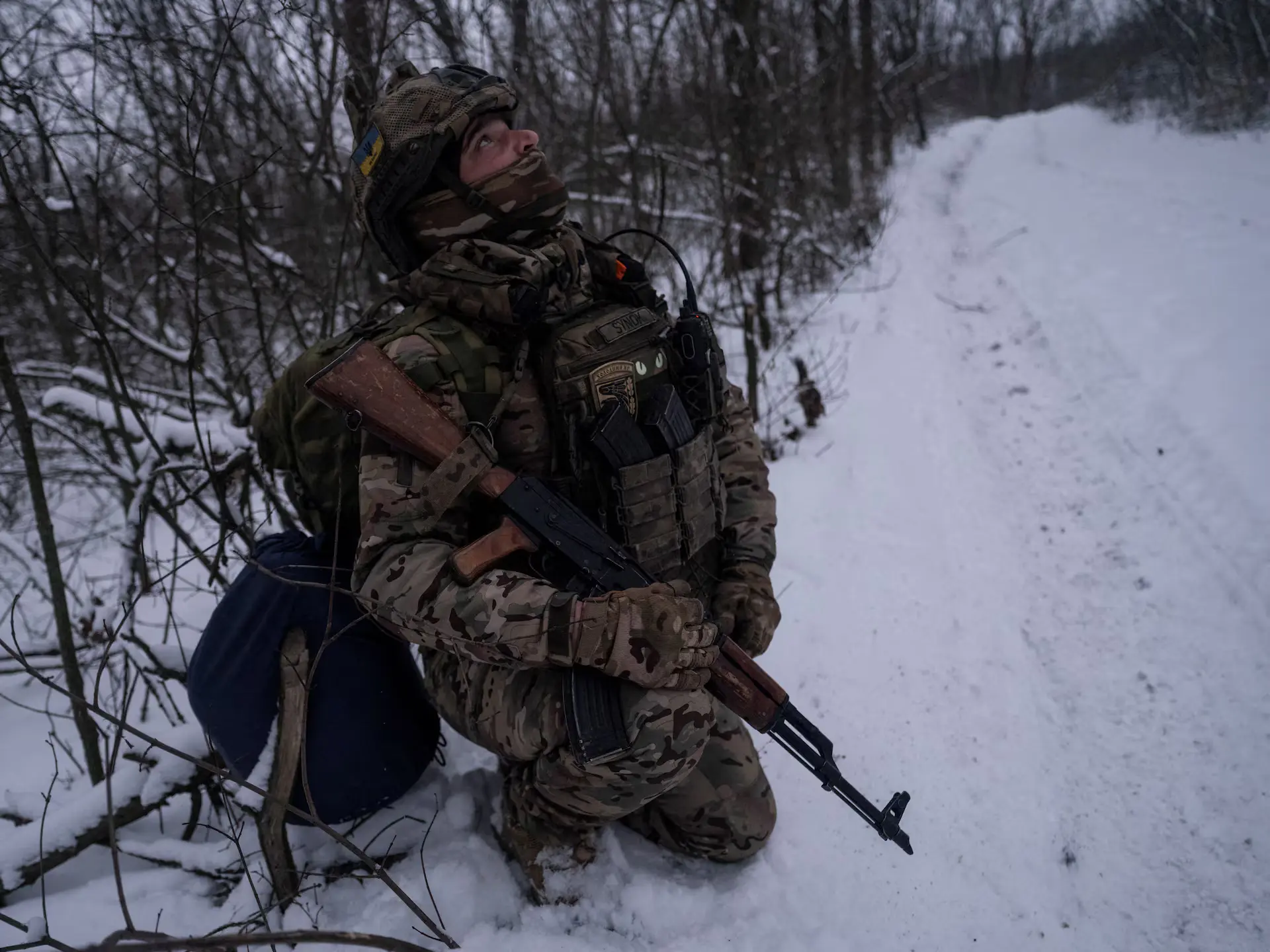 Ukrainian soldier kneeling in snow with rifle